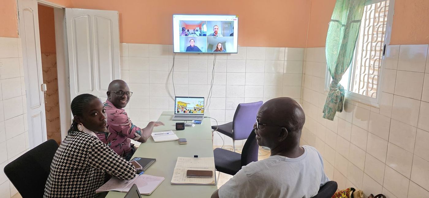 Réunion de travail autour d’une table, avec des participants en visioconférence sur l’écran