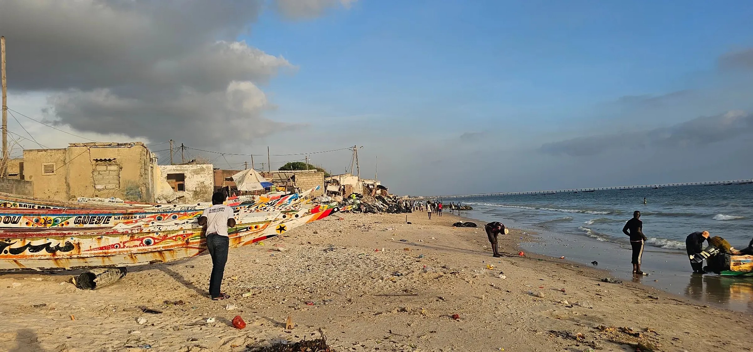Une plage de pêcheurs au Sénégal, des pirogues peintes à gauche et la mer à droite, en fin de journée
