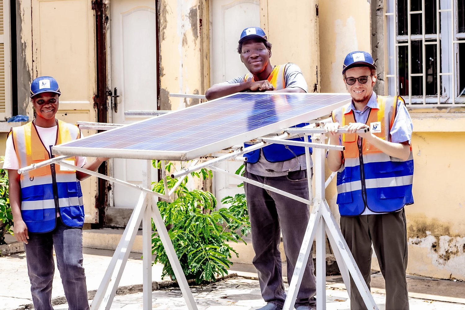 Trois stagiaires de Solar Perspectives, souriants, autour d’un panneau solaire posé sur son support