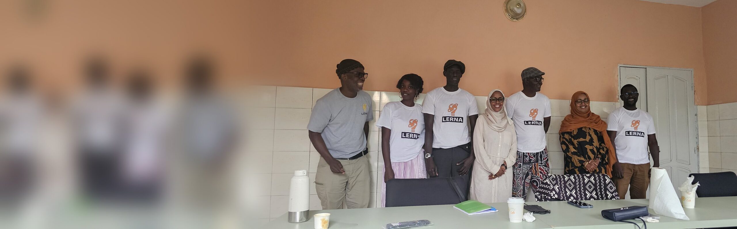 L’équipe de LERNA, en t-shirts de l’association, pose avec ses visiteuses dans la salle de réunion du bureau