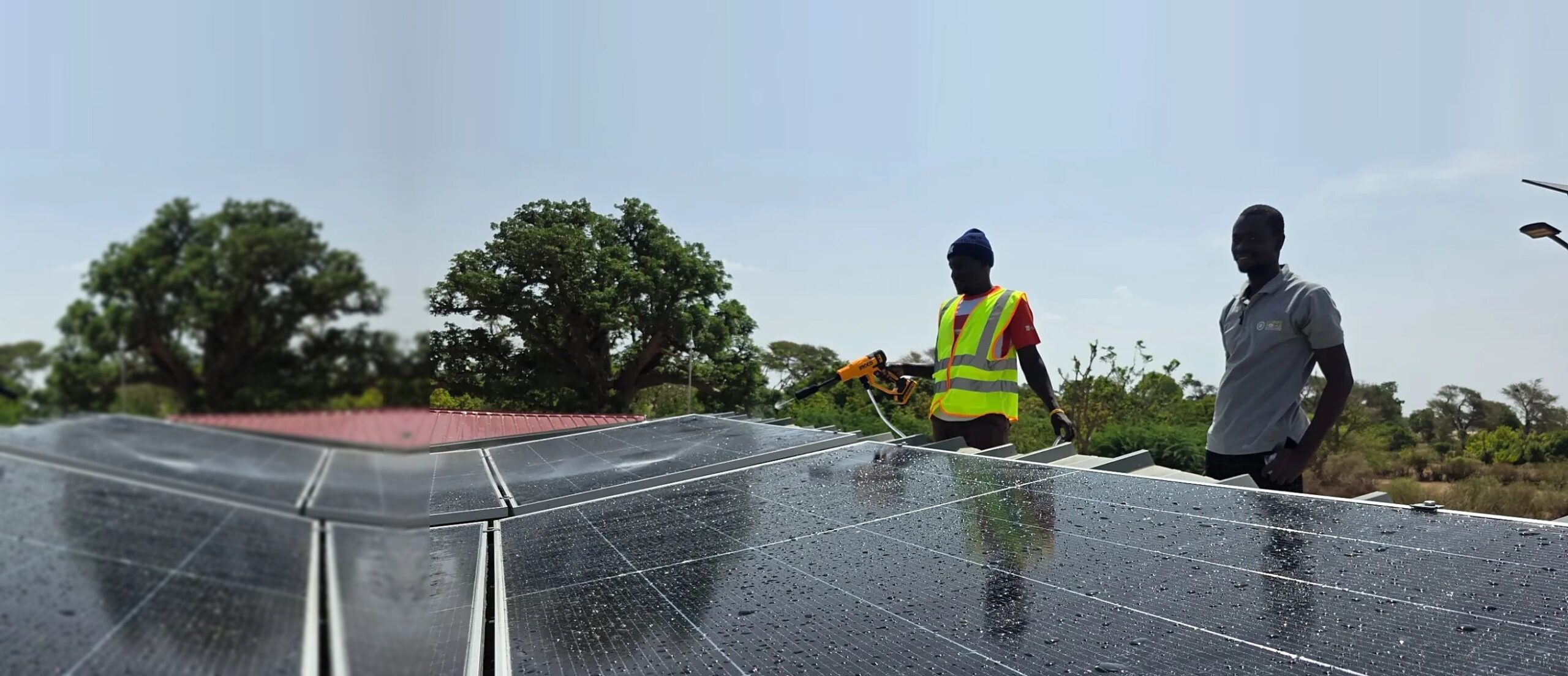 Deux techniciens nettoient au jet des panneaux solaires sur un toit, au milieu des arbres