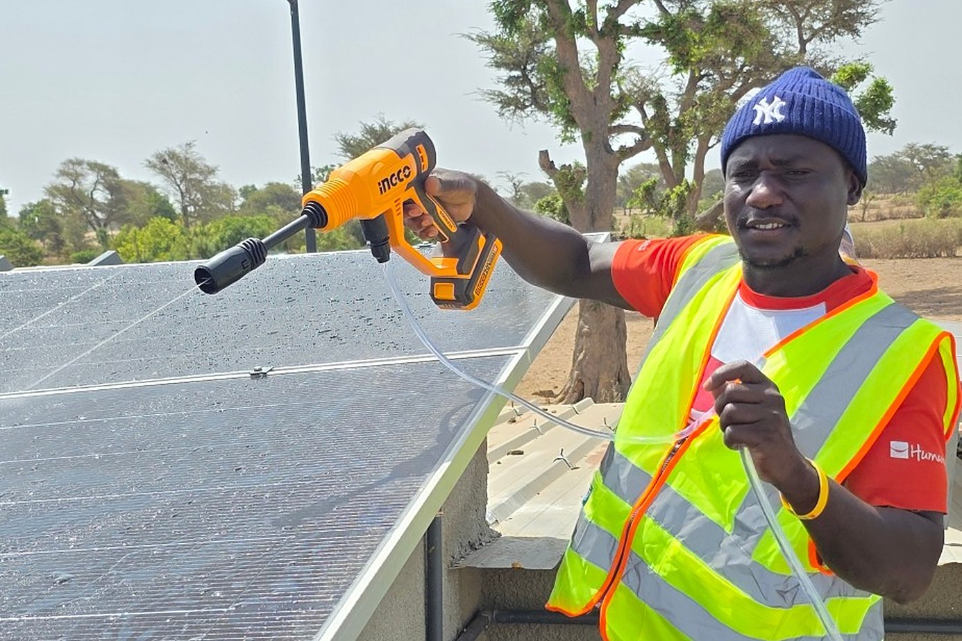 Un technicien en gilet nettoie au jet les panneaux solaires d’un poste de santé