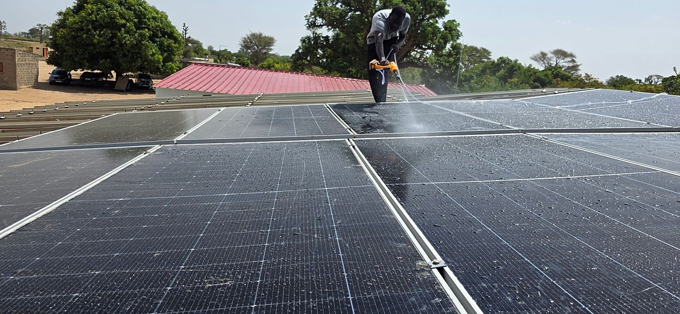 Un technicien nettoie au jet les panneaux solaires sur le toit d’un poste de santé