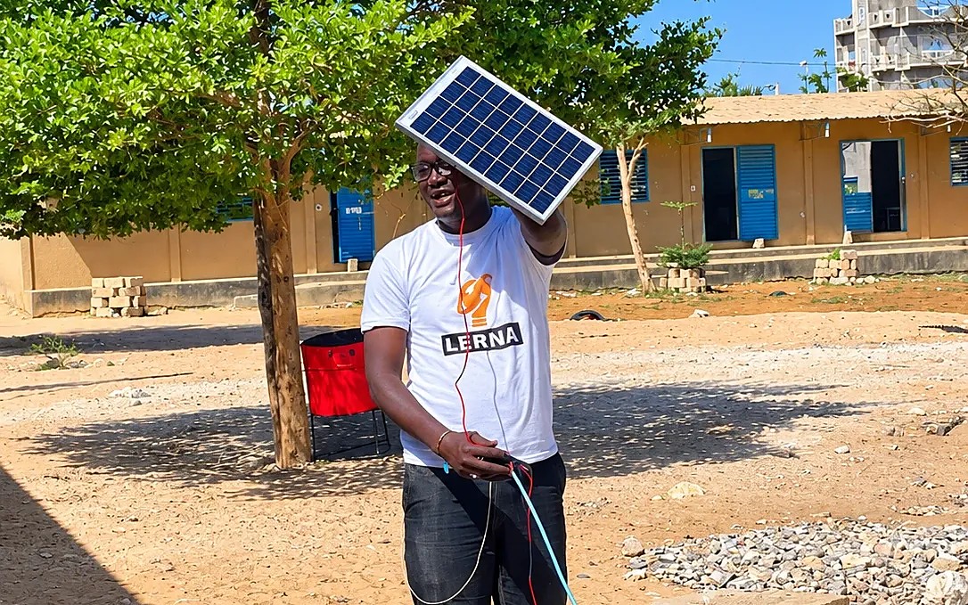 Un animateur de LERNA présente un petit panneau solaire en plein air, dans la cour d’une école