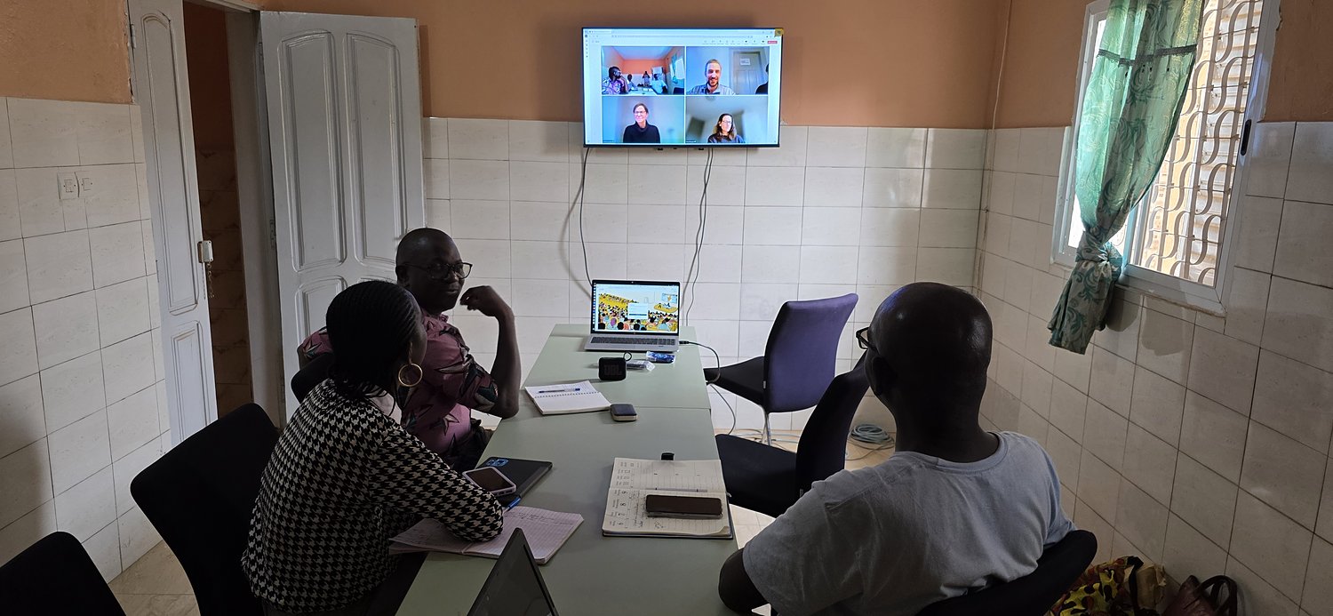 Réunion de travail autour d’une table, avec des participants en visioconférence