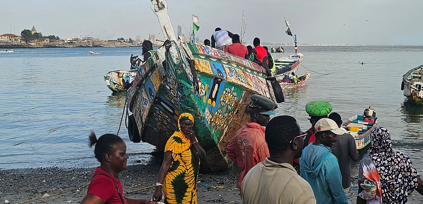 Des habitants sur une plage de pêcheurs, devant une grande pirogue peinte échouée