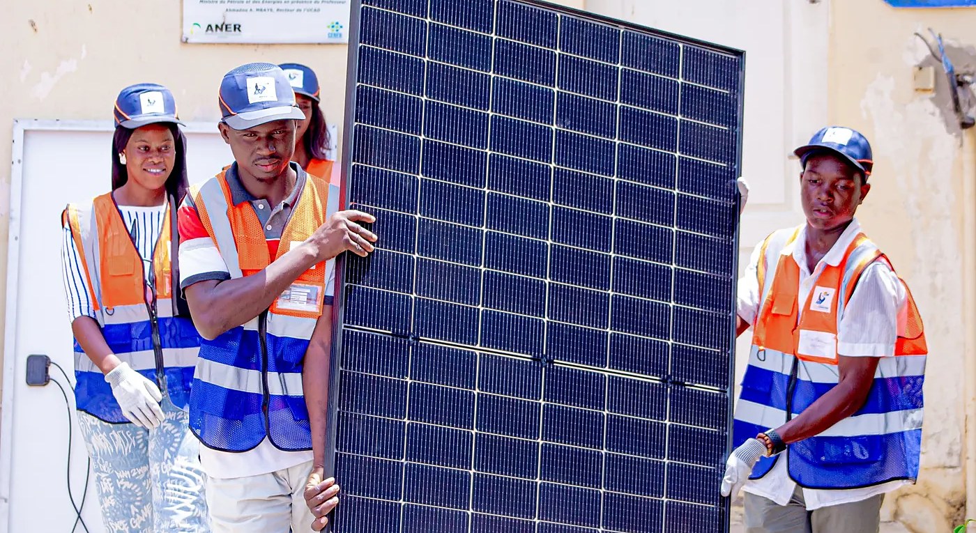 Des stagiaires portent un panneau solaire devant le laboratoire du CERER